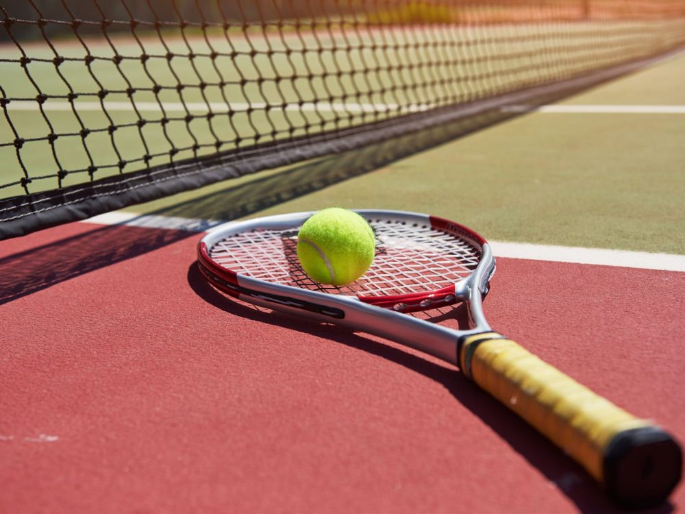 A tennis racket and new tennis ball on a freshly painted tennis court